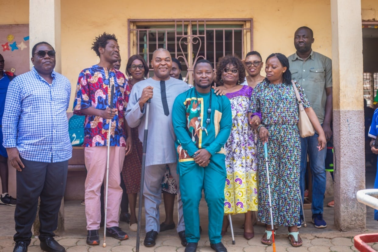 Group photograph outside a building: about eleven members in colourful dress, three white canes clearly visible.