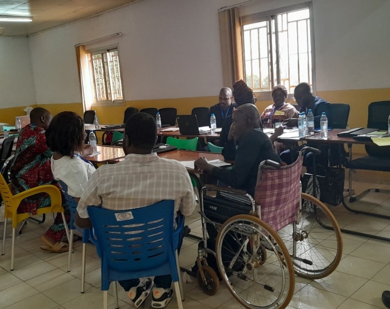 Workshop room: participants seated at tables taking notes, a wheelchair user in the foreground.