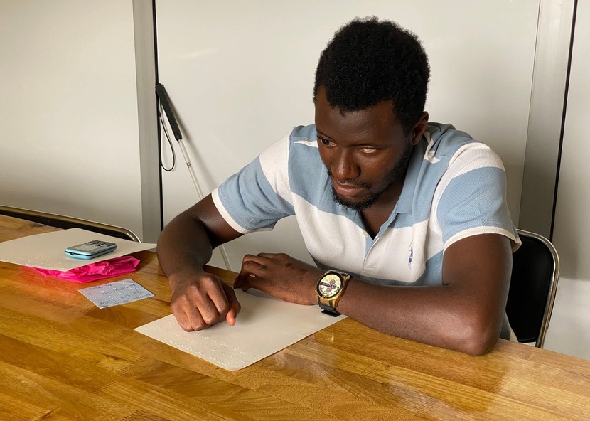 A Braille learner writing on a slate at a wooden table.