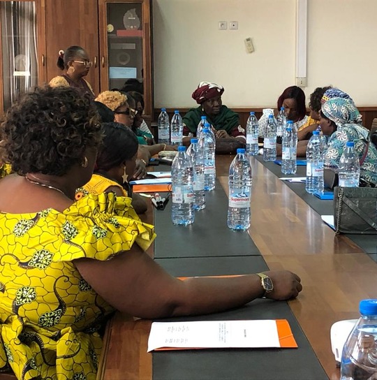 Women seated along a meeting table, one writing in the foreground.