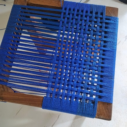 A stool seat part-woven with blue cord, seen from above.