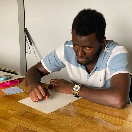 A Braille learner writing on a slate at a wooden table.