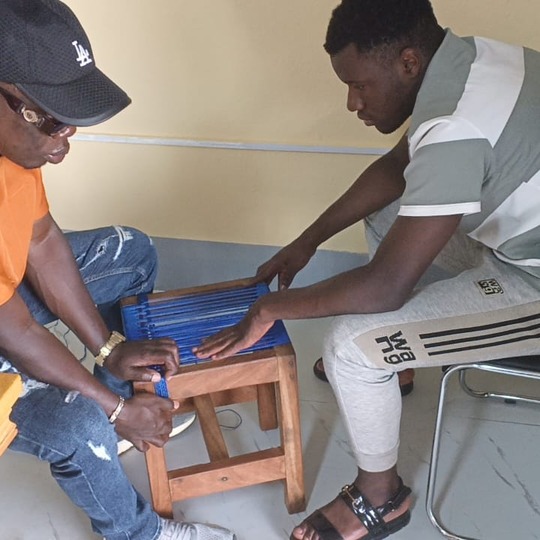 Two men weaving a stool seat with blue cord at the CAMAB Centre.