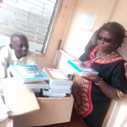 A woman in dark glasses and a colleague beside an open carton of new textbooks.