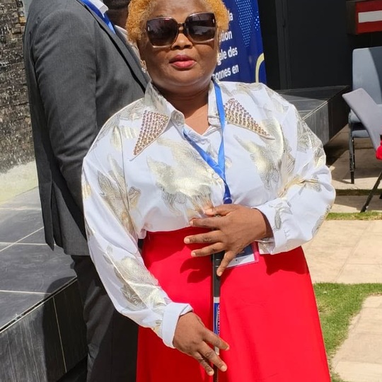 Eveline Angonwi, President of CAMAB Women, holding a white cane at a conference.