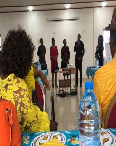 Conference hall, delegates standing at their places facing the front; banners at the side.
