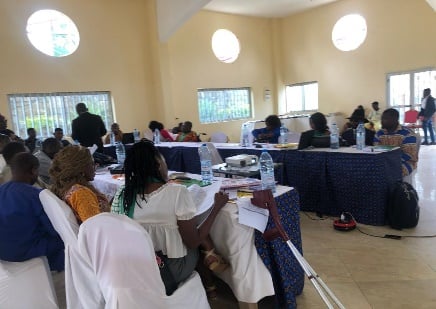 Workshop room seen from the back; participants seated at round tables, a white cane visible.