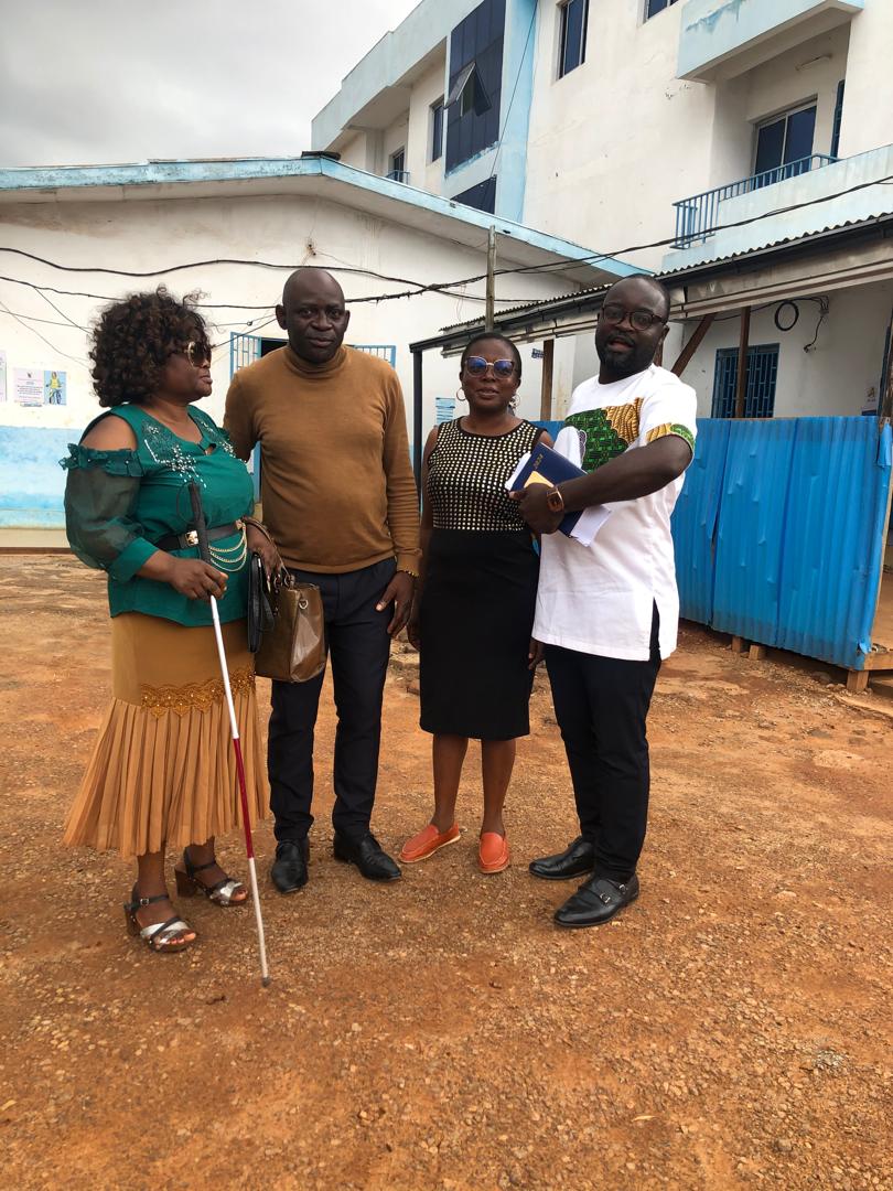 Four people outdoors in a yard: a woman with a white cane at the left, three others beside her.