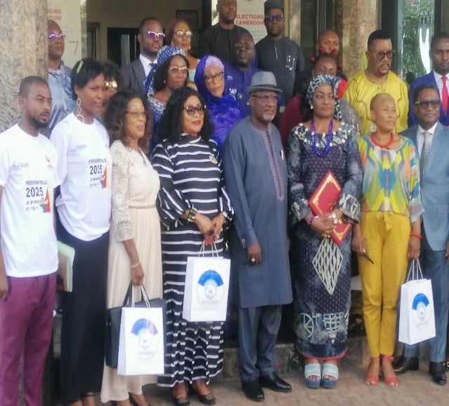 Group standing indoors holding branded gift bags; some wear event T-shirts marked 2025.