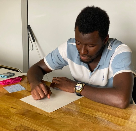 A learner writing Braille on a slate at a wooden table.
