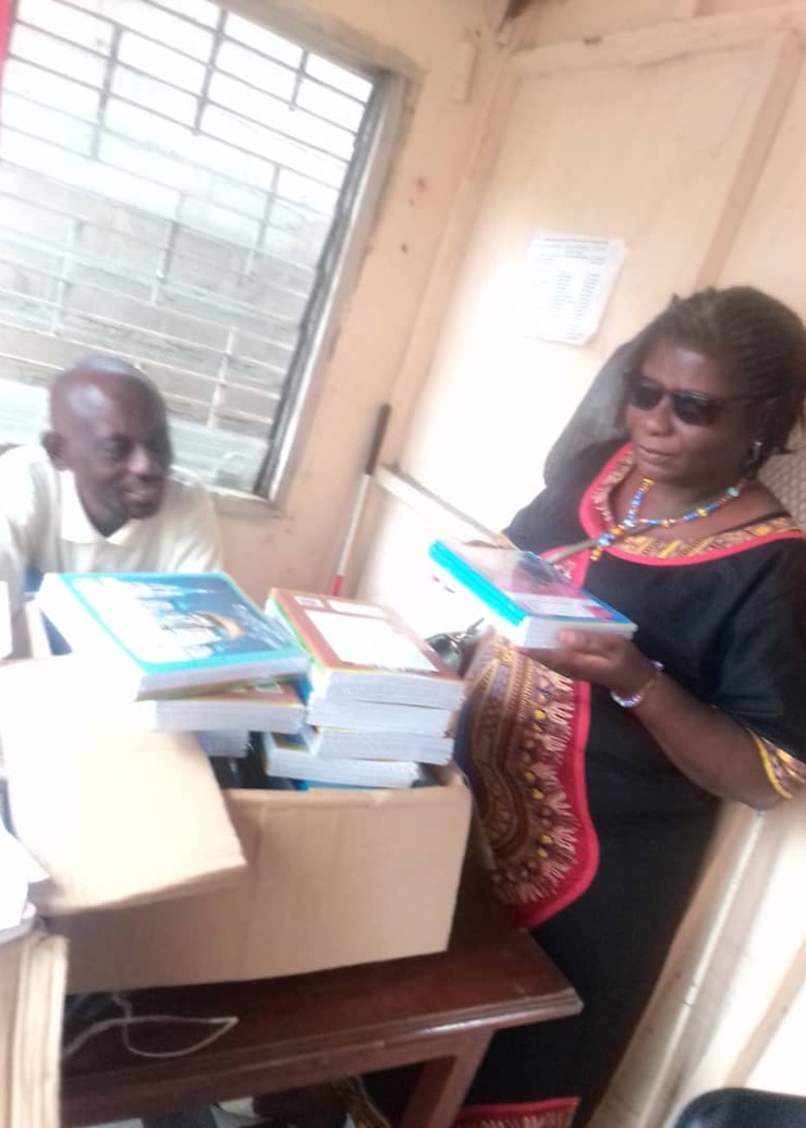 A woman in dark glasses and a colleague beside an open carton of new textbooks.