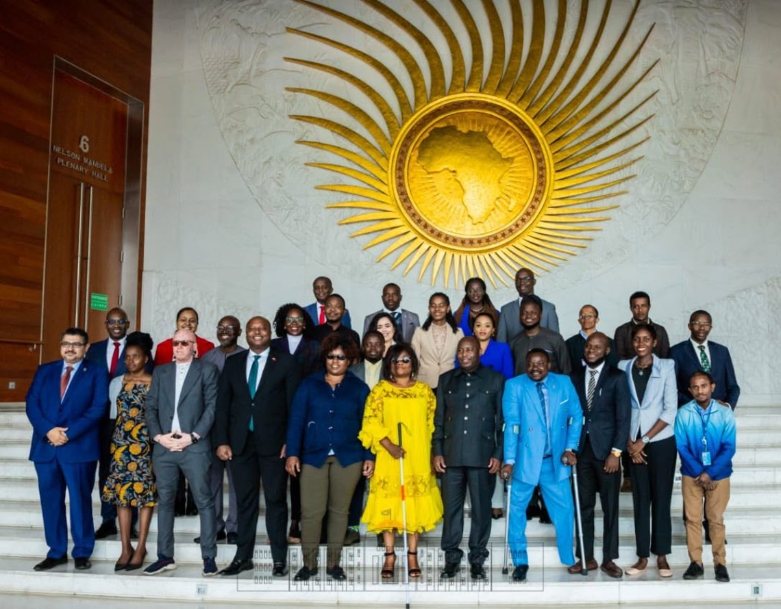 A delegation on the steps of the African Union plenary hall beneath the gold African Union emblem.